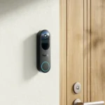 Vue large de la sonnette vidéo Reolink Doorbell Battery sur un mur blanc près d'une porte en bois
